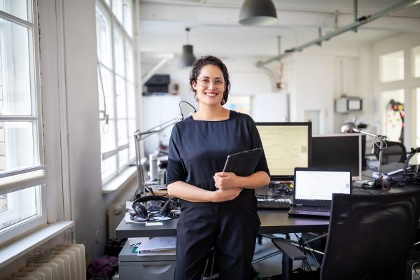 Beautiful female professional standing at modern workplace Portrait of a confident mature businesswoman holding a digital tablet in office. Beautiful female professional standing at modern workplace.